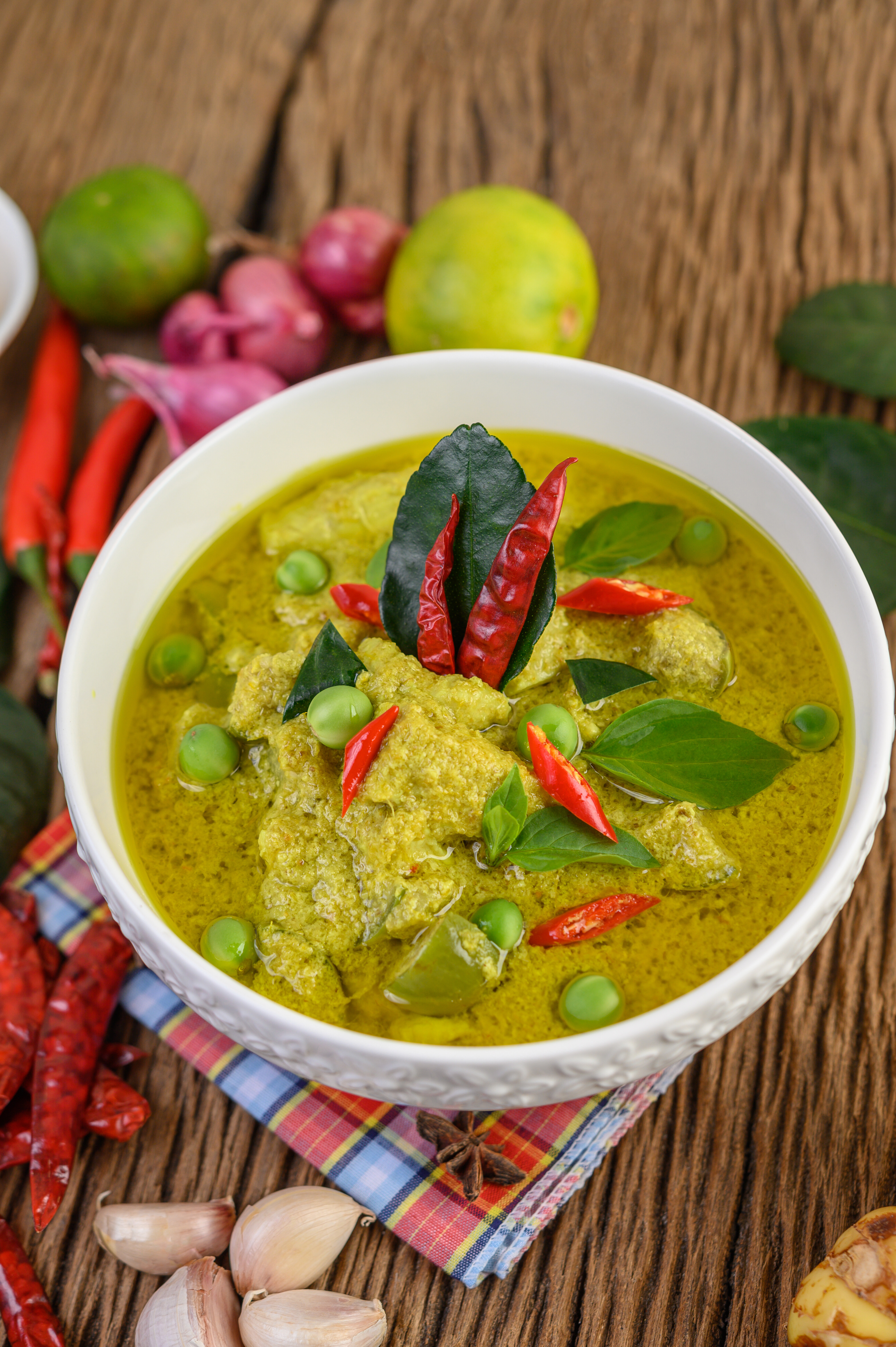 Vibrant green curry served in a bowl, garnished with fresh lime slices, red onion, lemongrass, garlic, and kaffir lime leaves, creating a fragrant and colourful dish